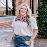 Woman with blonde hair standing in a front profile position wearing the Reece Top on campus. The focal point of this image is the embroidery on chest and lighting. The model paired this top with dark-wash denim shorts. 