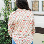 Woman with dark hair wearing a long-sleeve red and blue floral graphic shirt. Model paired this top with dark-wash denim jeans. 