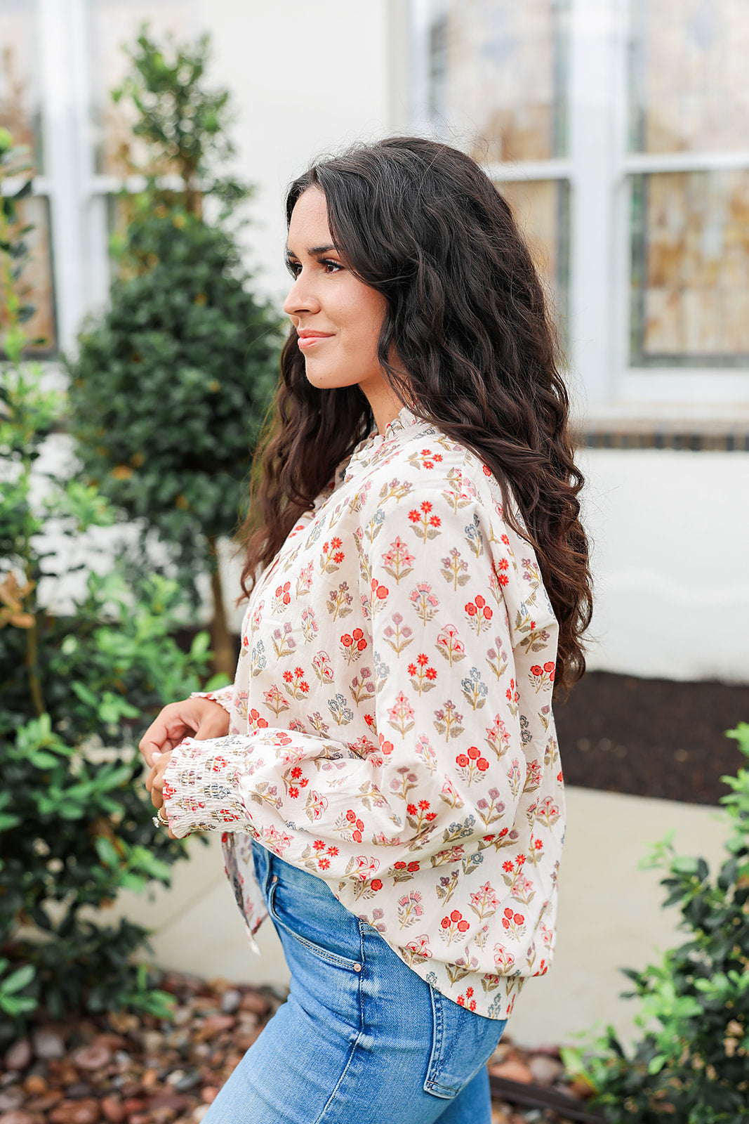 Woman with dark hair wearing a long-sleeve red and blue floral graphic shirt. Model paired this top with dark-wash denim jeans. 