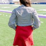 Woman with dark hair standing in a back profile position wearing the Sadie Top in a lifestyle scene. The focal point of this image is the black gingham pattern on back of top. The model paired this top with a red skirt.