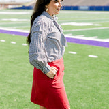 Woman with dark hair standing in a side profile position wearing the Sadie Top in a lifestyle scene. The focal point of this image is the black gingham pattern as well the bow on front of top. The model paired this top with a red skirt.