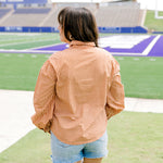 Woman with dark hair wearing a burnt orange gingham long-sleeve top, and light-wash denim shorts. 