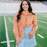 Woman with dark hair wearing a burnt orange gingham long-sleeve top, and light-wash denim shorts. 