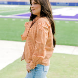 Woman with dark hair wearing a burnt orange gingham long-sleeve top, and light-wash denim shorts. 