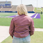 Woman with blonde hair standing in a back profile position wearing the Sadie Top in a lifestyle scene. The focal point of this image is the maroon gingham pattern on back of long-sleeve top. The model paired this top with light-wash denim shorts. 