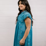 Woman wearing a blue dress against a white background facing the side.
