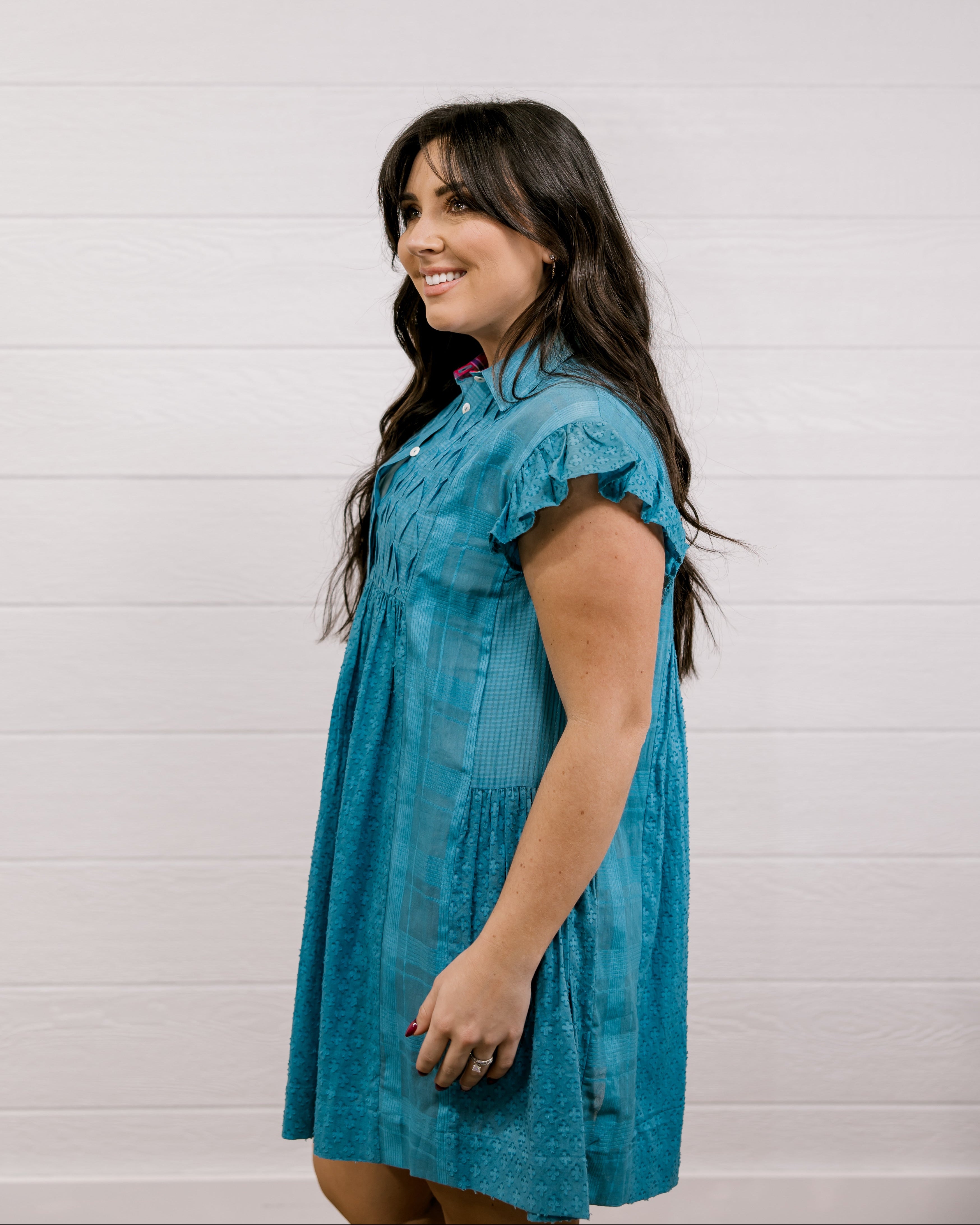 Woman wearing a blue dress against a white background facing the side.