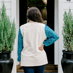 Woman with dark hair wearing a sweatshirt with turquoise sparkle sleeves & embroidery on front that says "Jesus Is The Reason". Model paired this top with dark-wash denim jeans. 