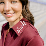 Woman with dark hair wearing a maroon dress with a close-up on howdy embroidery. 