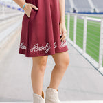 Woman wearing a midi maroon dress with howdy embroidered in white. The model paired this dress with cream boots. 