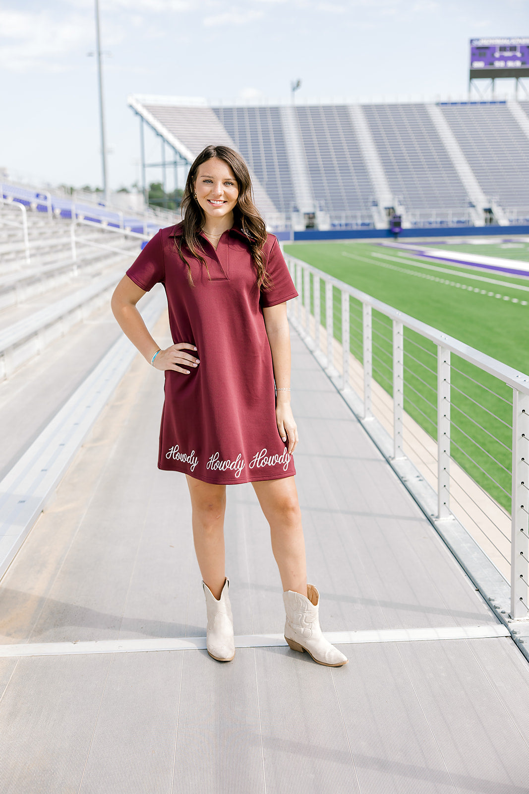 Woman with dark hair wearing a maroon midi dress with white embroidery along bottom, and cream colored boots. 