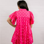 Person wearing a pink polka dot dress against a white background facing back.