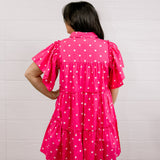 Person wearing a pink polka dot dress against a white background facing back.