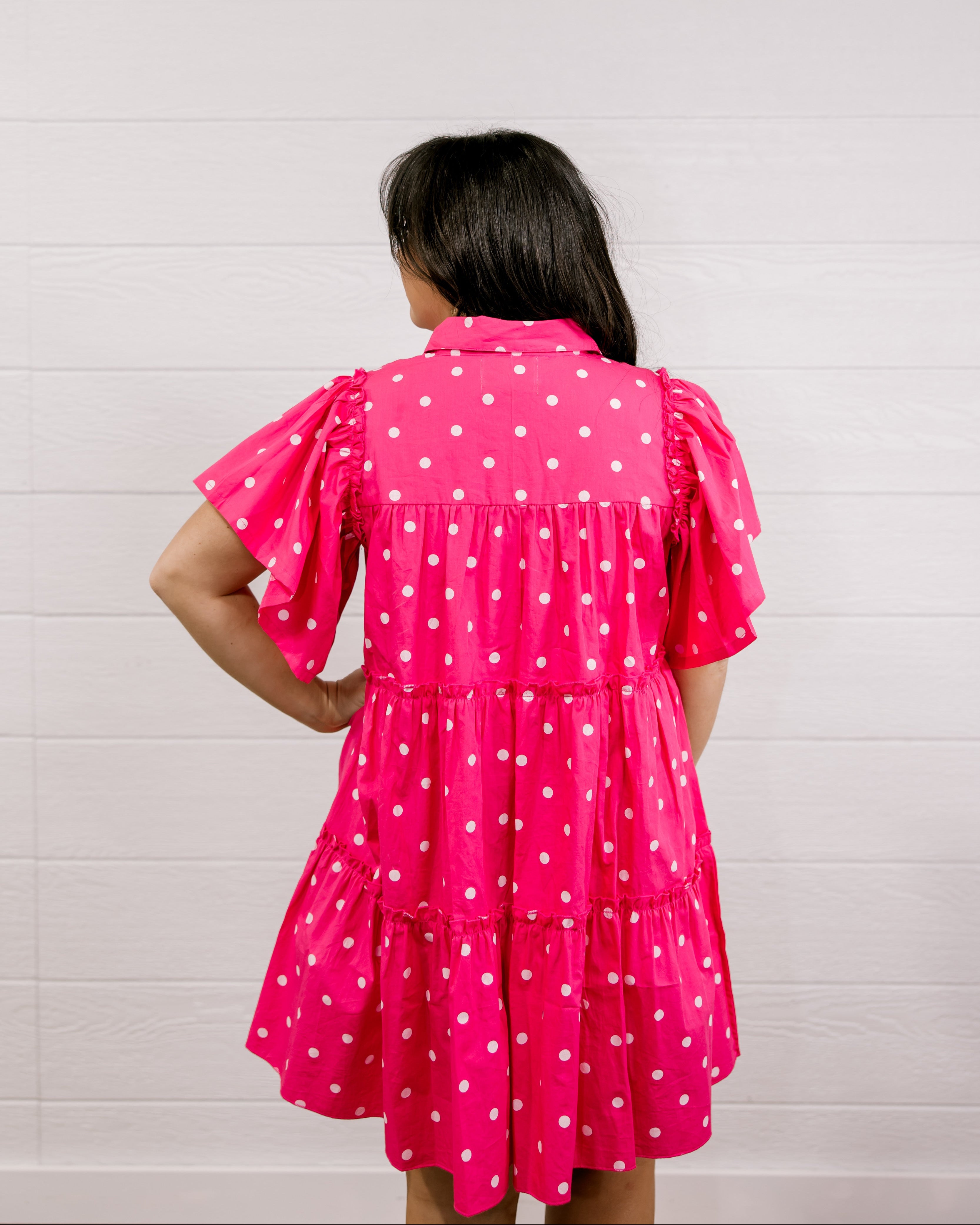 Person wearing a pink polka dot dress against a white background facing back.