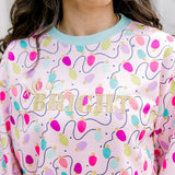Woman with dark hair wearing a sweatshirt with Christmas light graphics  that are multi-colored. Model paired this top with dark-wash denim jeans. 