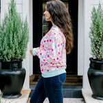 Woman with dark hair wearing a sweatshirt with Christmas light graphics  that are multi-colored. Model paired this top with dark-wash denim jeans. 