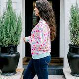 Woman with dark hair wearing a sweatshirt with Christmas light graphics  that are multi-colored. Model paired this top with dark-wash denim jeans. 
