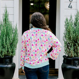 Woman with dark hair wearing a sweatshirt with Christmas light graphics  that are multi-colored. Model paired this top with dark-wash denim jeans. 
