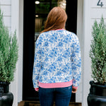 Woman with red hair wearing a blue floral sweatshirt with pink accents and "Merry Christmas" embroidered on front. Model paired this top with denim jeans. 