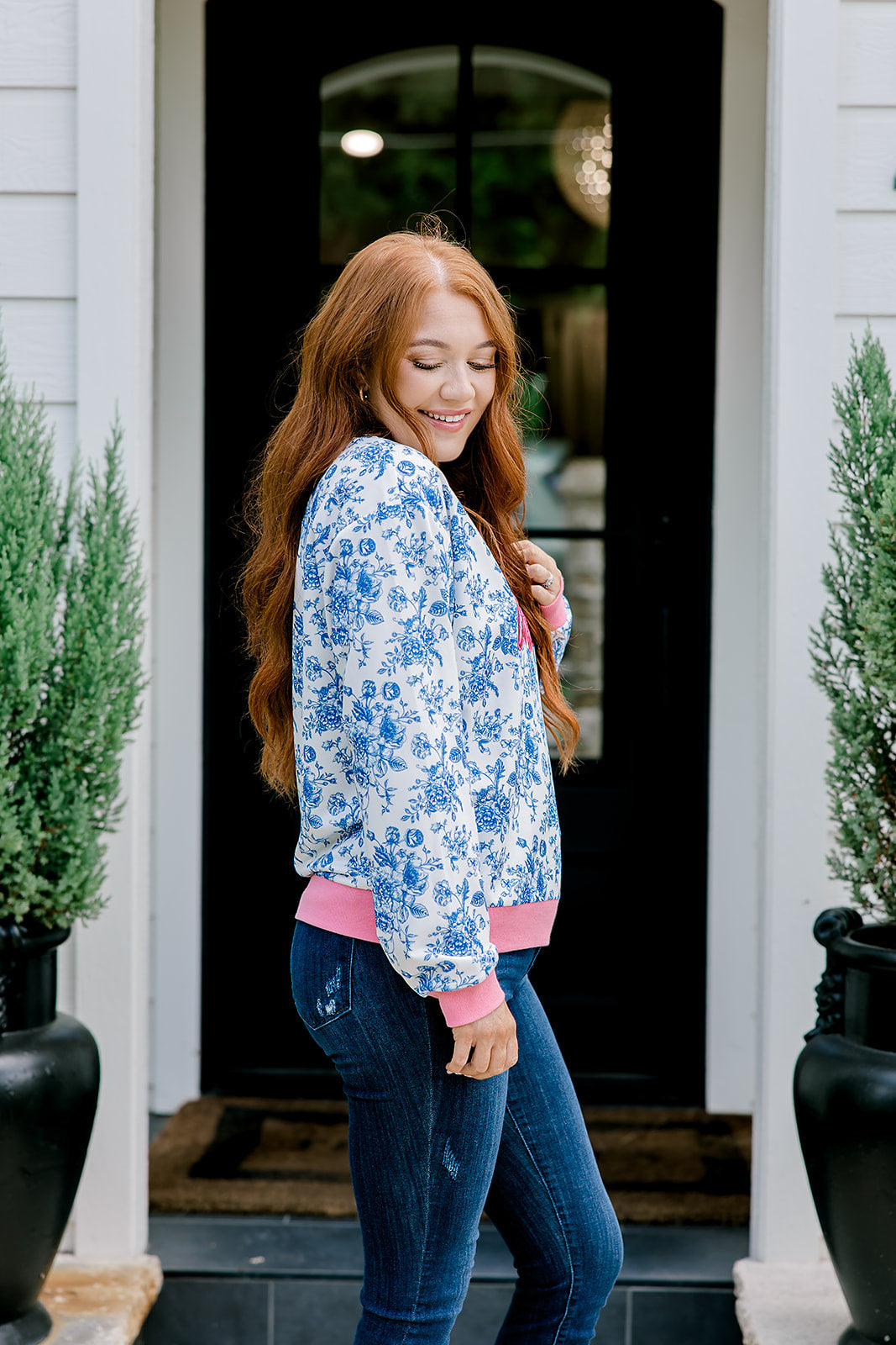 Woman with red hair wearing a blue floral sweatshirt with pink accents and "Merry Christmas" embroidered on front. Model paired this top with denim jeans. 