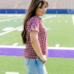 Woman with dark hair standing in a side profile position wearing the Stevie Top in a lifestyle scene. The focal point of this image is the striped ruffle sleeves as well as length of shirt and flower graphics. The model paired this tip with light-wash denim shorts. 