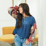 Woman with dark hair standing in a front profile position wearing the Tammy Top in a lifestyle scene. The focal point of this image is the waffle knit fabric and puffy sleeves. The model paired this top with mid-wash denim jeans. 