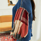Woman with dark hair standing in a side profile position wearing the Tammy Top in a lifestyle scene. The focal point of this image is the ruffled plaid red sleeves. The model paired this top with mid-wash denim jeans. 