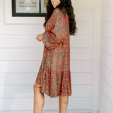Woman with dark hair wearing a red/green otomi graphic dress that is long-sleeve & has slight ruffle at bottom of dress.