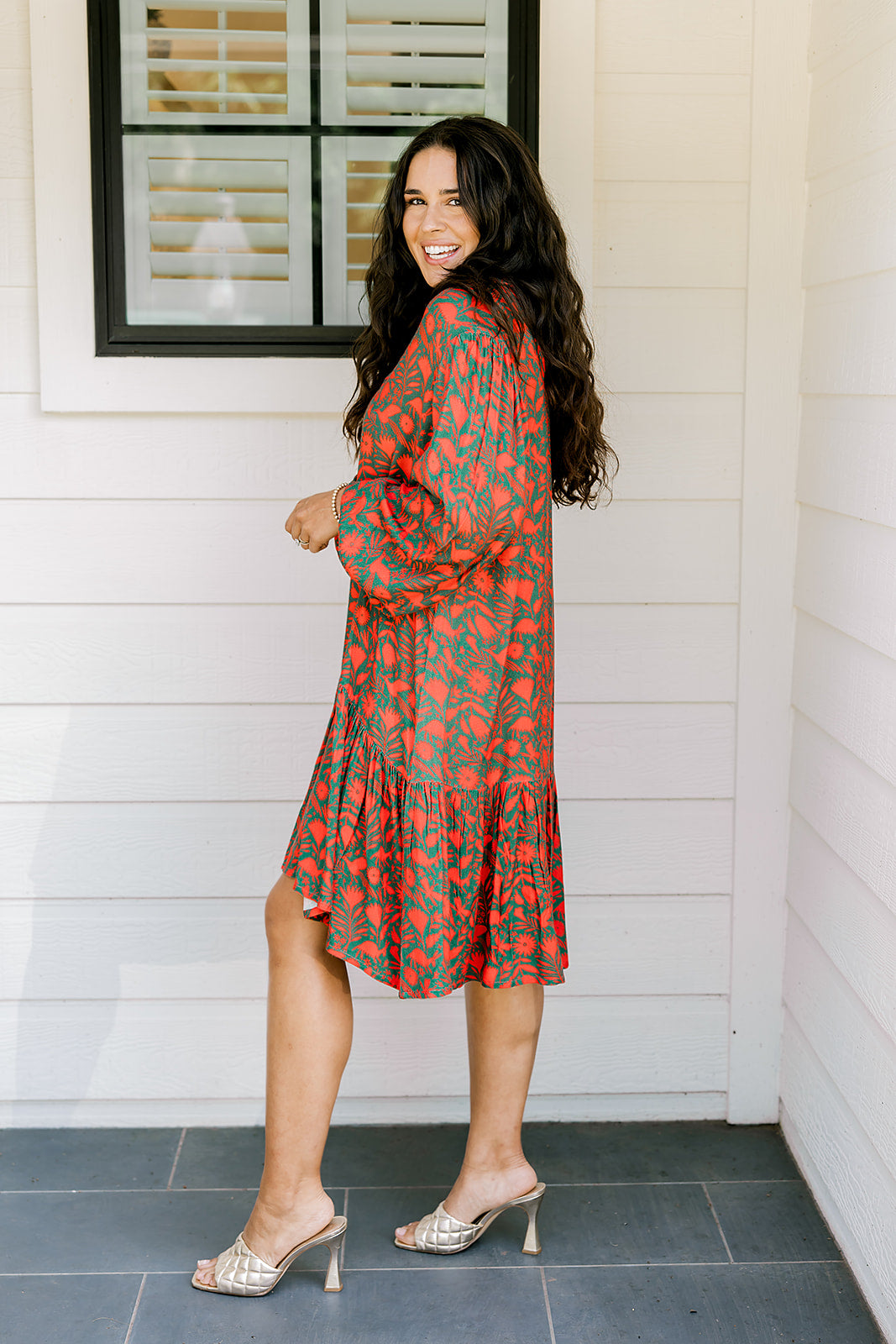 Woman with dark hair wearing a red/green otomi graphic dress that is long-sleeve & has slight ruffle at bottom of dress.