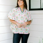 Woman with dark hair wearing a top in the Tori body style featuring pink & green nutcracker graphics. Model paired this top with faux leather leggings.