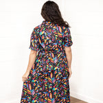 Woman with dark hair in a back profile position wearing the Vanessa Dress against a while background. The focal point of this image is the graphics on the back of the dress with small emphasis on belt and back of sleeves. 