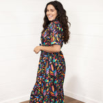 Woman with dark hair in a side profile position wearing the Vanessa Dress against a white background. The focal point of this image is the graphics on side of dress with emphasis on the sleeve area. 