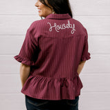 Woman wearing a maroon ruffled shirt with 'Howdy' embroidered on the back against a white background
