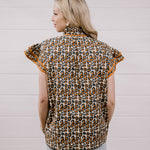 A woman shown from the back wearing a leopard print short-sleeve blouse with ruffled sleeves and light blue jeans, standing against a white paneled wall.