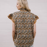 A woman shown from the back wearing a leopard print short-sleeve blouse with ruffled sleeves and light blue jeans, standing against a white paneled wall.