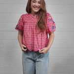 Video of woman wearing colorful pink top in front of white wall. front facing, side facing, and back facing