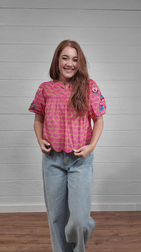 Video of woman wearing colorful pink top in front of white wall. front facing, side facing, and back facing
