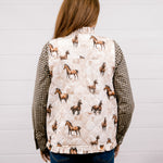A woman viewed from behind wearing a quilted vest with a horse print on the back panel and checkered sleeves, paired with blue jeans, against a white wood-paneled wall.
